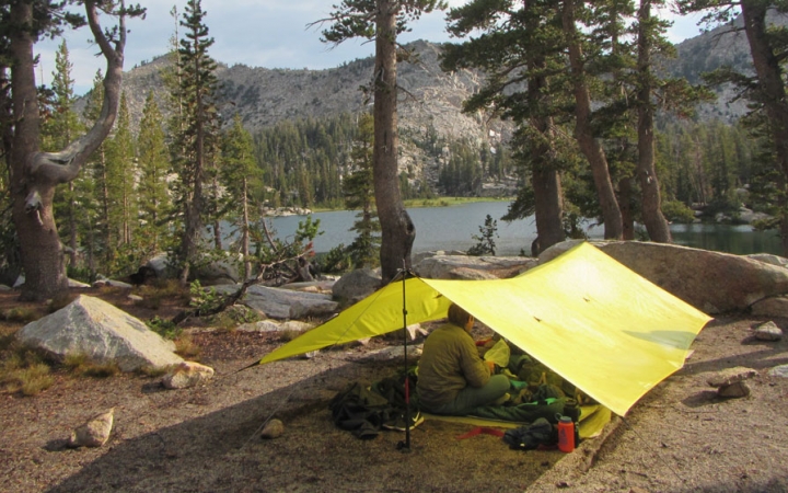 a person rests under a tarp shelter near a body of water on an outward bound course for bipoc